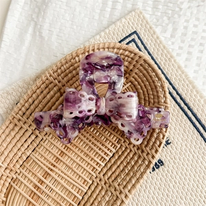 Detailed view of a purple marble bow claw clip with handmade gold tag on a woven tray