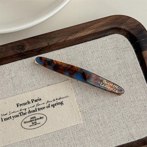 Detailed close-up of marble acetate hair barrette with gold logo on a wooden display tray