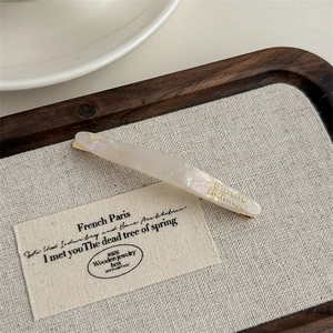 Detailed close-up of crescent acetate barrette in pearlescent white with gold lettering