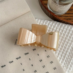 Dettaglio di un fermaglio per capelli a fiocco color champagne con trame fini e logo YD in metallo