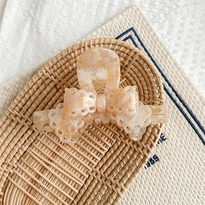 Macro detail of peach marble textured bow hair claw clip with delicate lace hollow edges