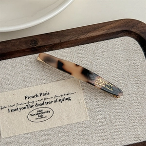 Detailed close-up of tortoise shell acetate hair clip with golden metallic logo lettering