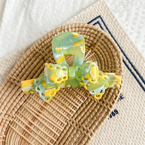 Detail showing the green and yellow marble texture bow hair claw with handmade logo