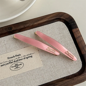 Detail view of two pink acetate hair barrettes with gold engraving on a wooden tray