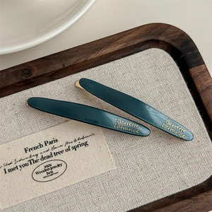 Detailed top view of dark green acetate hair clip with gold logo on a wooden tray
