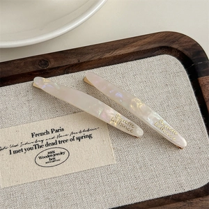 Detail of two acetate hair clips with gold lettering on a wooden display tray