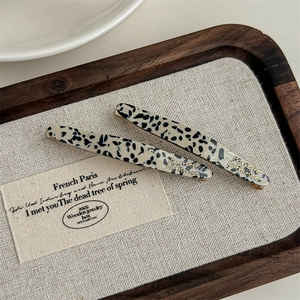 Detail of tortoiseshell pattern hair clips with gold logo on a wooden tray