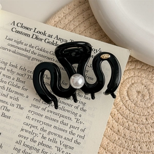 Detail of glossy black wave-shaped hair claw clip with white pearl and gold logo accent