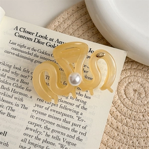 Detailed view of an amber wavy hair claw clip with a white pearl and gold metal logo