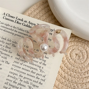 Detail of pink marble hair claw with pearl accent and gold logo on book pages