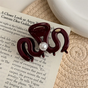 Detail view of burgundy wavy hair claw clip with pearl on vintage book background