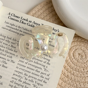 Iridescent wavy hair claw clip featuring large pearl and golden detail on fashion magazine