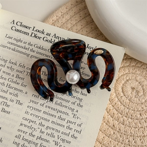 Close-up of tortoiseshell hair claw clip with cream pearl and gold logo on vintage magazine