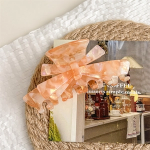 Close-up of orange marble acetate bow hair claw clip on a rustic decorative background
