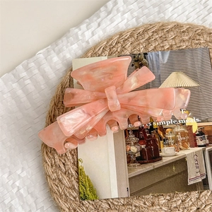 Pink marble acetate bow hair claw clip displayed on a natural woven mat with a magazine
