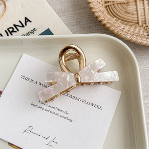 Detail of elegant gold bow hair claw clip with pearlescent finish in a tray
