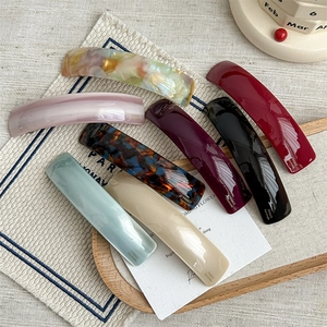 Curved acetate spring hair clips in various marble and solid colors on a wooden tray