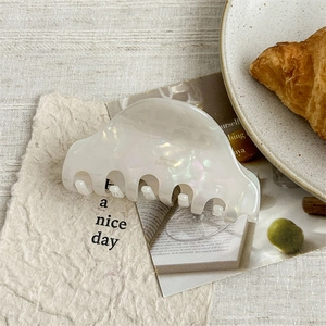 Close-up of cream acetate hair claw clip with golden logo in a French vintage setting