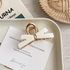 Detail of elegant cream bow hair claw clip on white ceramic plate with golden accents