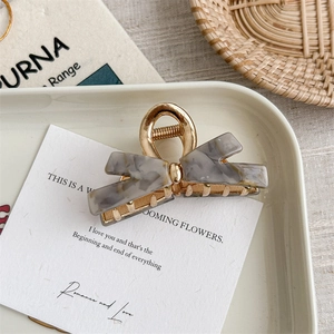 Detail of elegant gold metal bow hair claw with marble pattern acrylic on white tray