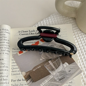 Detailed view of glossy black hair claw clip with burgundy trim and gold logo detail