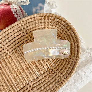 Detailed macro view of an elegant pearl acetic acid hair claw clip on a rustic tray
