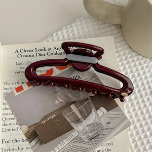 Detailed view of hollow oval burgundy shark hair clip on a minimalist background