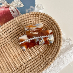Detail of amber tortoiseshell claw clip with pearls on a rustic wicker tray background