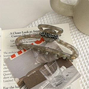 Detail of taupe marble acetate hair claw clip with checkerboard accent and gold logo