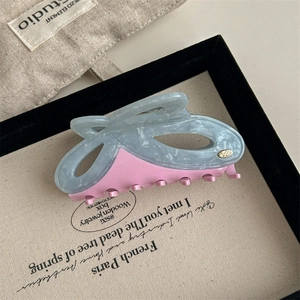 Detail of large acetate hair claw clip in bicolor pink and marbled blue with golden logo
