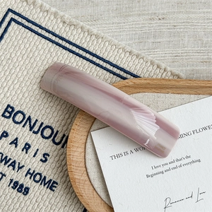 Macro shot of pink marble pattern acetate hair clip with gold logo on wooden tray