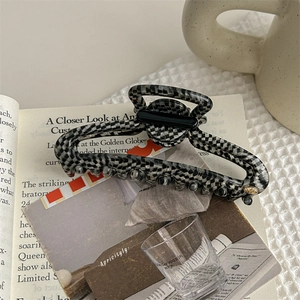 Detail of checkered hair claw clip with golden logo button on a stylish lifestyle background