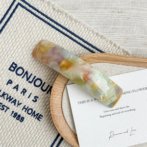 Detail of curved acetate hair clip with multicolored marble texture on a beige fabric