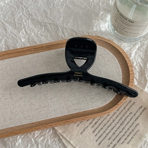Macro detail of French handmade black hair claw clip with golden lettering on wood tray
