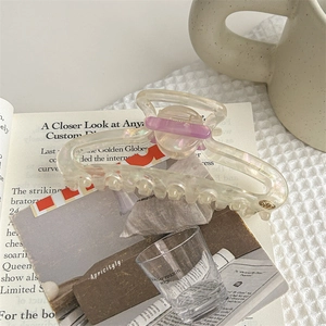 Iridescent acrylic hair claw clip with purple accent displayed on an open book