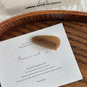 Detailed macro view of dark brown acetate teardrop hair clip on vintage art paper