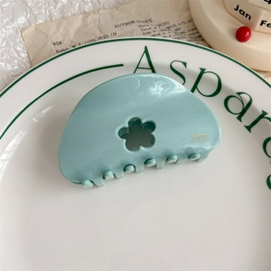 Detail of mint green acetate hair claw with hollow flower design and gold lettering