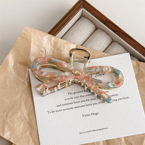 Detail view of colorful acetate bow hair claw clip with golden metal frame and marble pattern