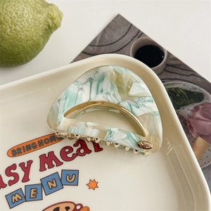 Detail of mint marble acetate hair claw clip with golden logo on a vintage ceramic plate