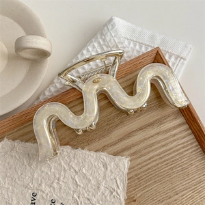 Detail of a large pearlescent white wavy hair claw clip with golden metal spring