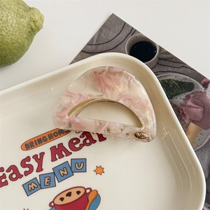 Detail view of pink marble acetate hair claw clip with golden spring on a white tray