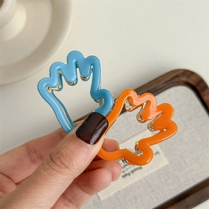 Pinces à cheveux ondulées en bleu et orange tenues à la main pour l'échelle réelle