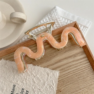 Macro detail of extra large wave hair claw clip in orange pink marble finish on a tray