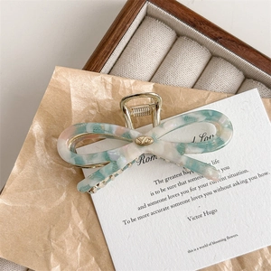 Detail view of acetate marble bow hair claw with elegant golden metal logo inlay