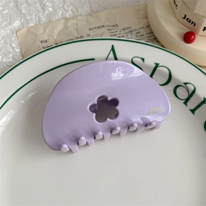 Close-up of a lavender floral hair claw clip with golden text detail on a white tray