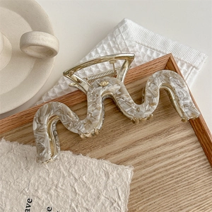 Detail showing marble wave hair claw clip on wooden tray with cozy minimalist background