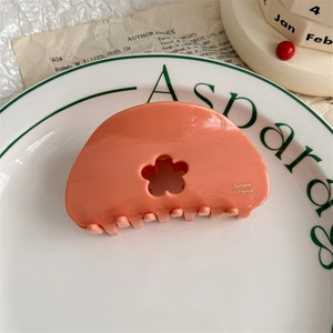 Detail of peach orange acetate flower hair claw clip resting in a white porcelain dish