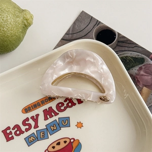 Detail of a semi-circular marble pattern hair claw with a small metal JD logo accent
