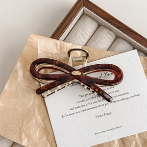 Detailed close-up of tortoise shell bow hair claw with gold spring and metallic accents