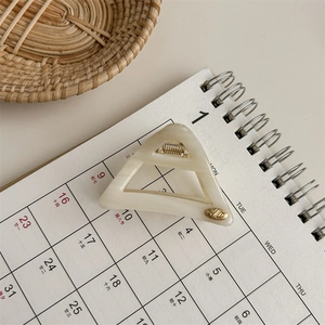 Close-up of cream acetate triangle hair claw clip with gold spring and metal emblem